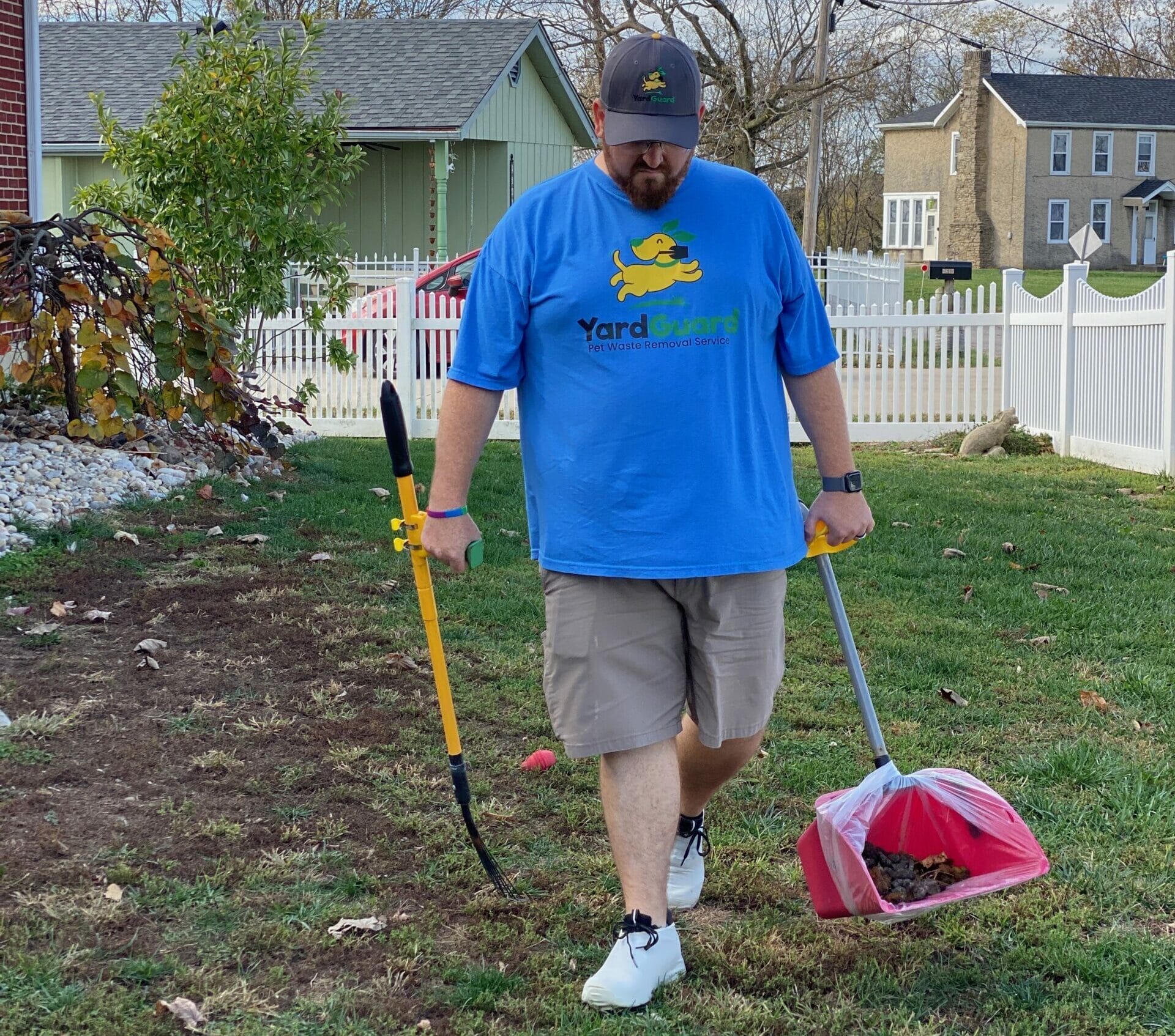 Employee of Yard Guard LLC in blue branded shirt performing dog waste removal in a residential yard.